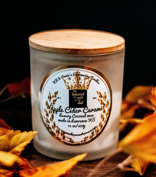 A close-up of the Apple Cider Caramel candle in a glass jar in a refined ambiance with a label that says KK & Annie's Empowering Candles, She believed she could so she did, with a golden Queen's crown.