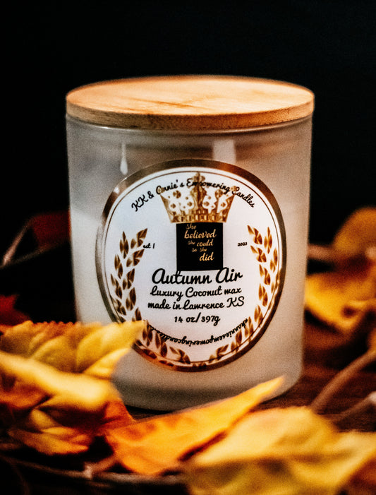 A close-up of the Autumn Air candle in a glass jar in a refined ambiance with a label that says KK & Annie's Empowering Candles, She believed she could so she did, with a golden Queen's crown.