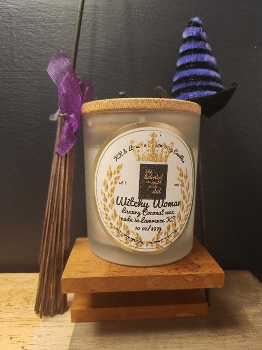 A close-up of the Witchy Women candle in a glass jar in a refined ambiance with a label that says KK & Annie's Empowering Candles, She believed she could so she did, with a golden Queen's crown.