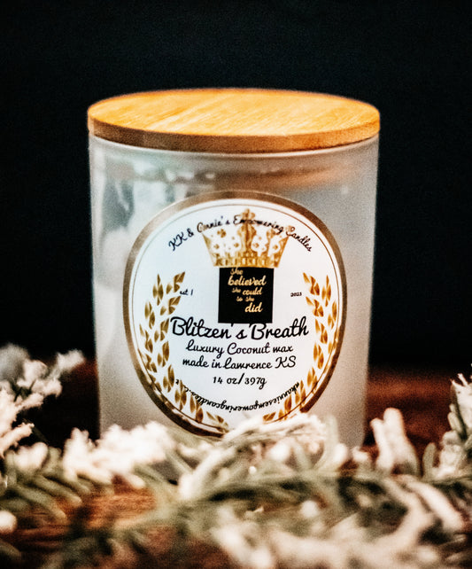 A close-up of the Blitzen's Breath holiday candle in a glass jar in a refined ambiance with a label that says KK & Annie's Empowering Candles, She believed she could so she did, with a golden Queen's crown.