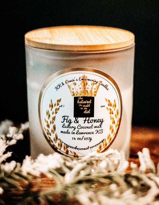 A close-up of the Fig & Honey candle in a glass jar in a refined ambiance with a label that says KK & Annie's Empowering Candles, She believed she could so she did, with a golden Queen's crown.