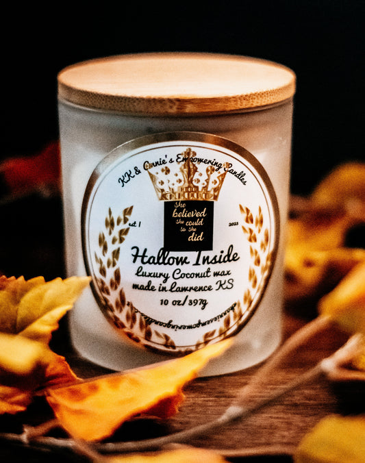 A close-up of the Hallow Inside Halloween candle in a glass jar in a refined ambiance with a label that says KK & Annie's Empowering Candles, She believed she could so she did, with a golden Queen's crown.