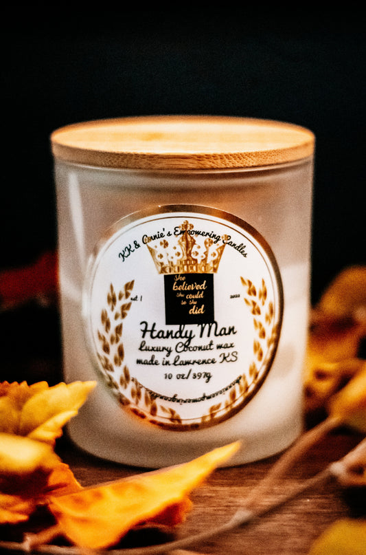 A close-up of the Handy Man luxury candle in a glass jar in a refined ambiance with a label that says KK & Annie's Empowering Candles, She believed she could so she did, with a golden Queen's crown.