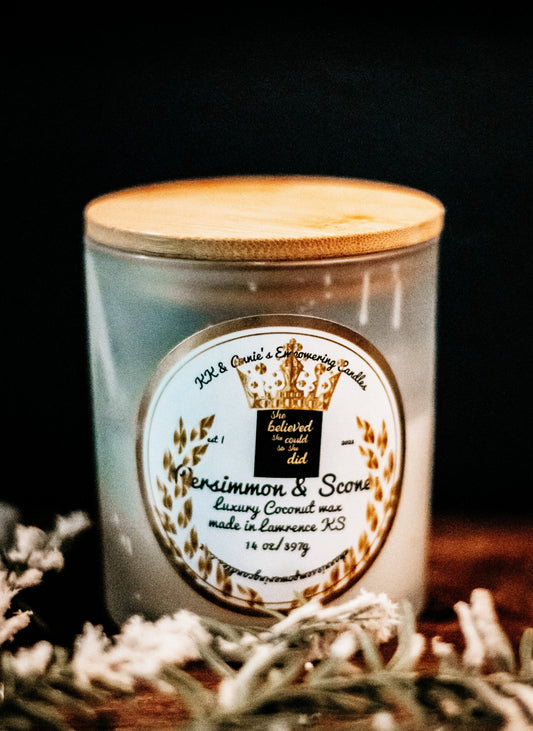 A close-up of the Persimmon & Scones candle in a glass jar in a refined ambiance with a label that says KK & Annie's Empowering Candles, She believed she could so she did, with a golden Queen's crown.