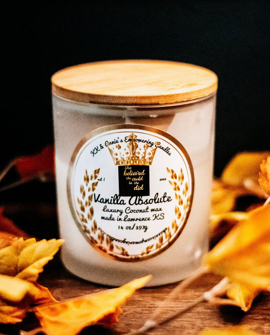 A close-up of the Vanilla Absolute luxury candle in a glass jar in a refined ambiance with a label that says KK & Annie's Empowering Candles, She believed she could so she did, with a golden Queen's crown.