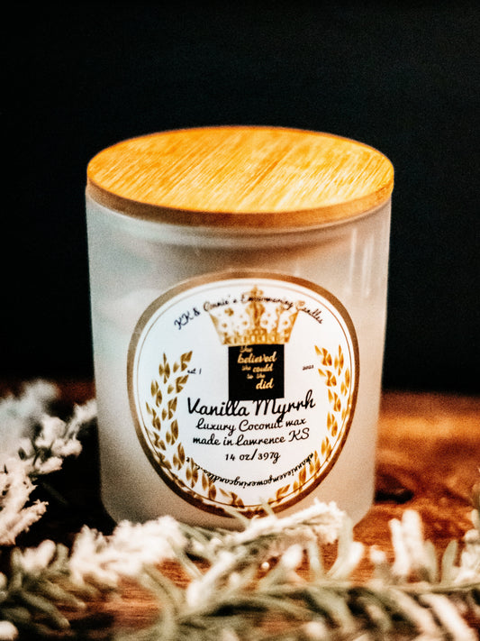 A close-up of the Vanilla Myrrh luxury candle in a glass jar in a refined ambiance with a label that says KK & Annie's Empowering Candles, She believed she could so she did, with a golden Queen's crown.